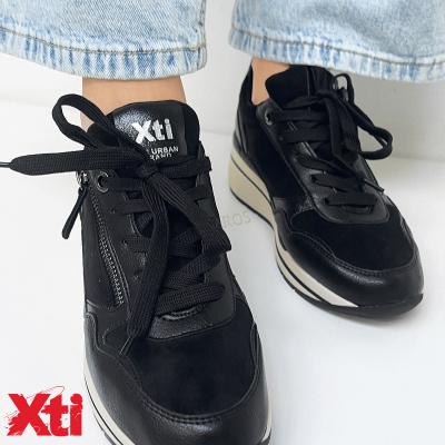 Ténis pretos Xti com cadarços e fecho de correr lateral usados com jeans claros.