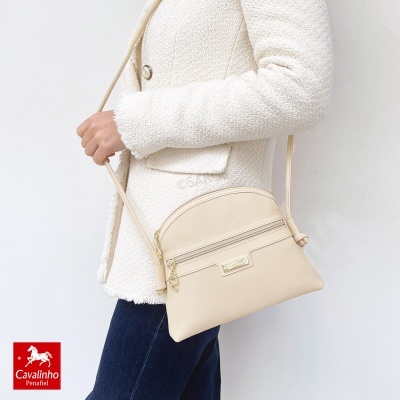 Mala de ombro bege com fecho dourado e logótipo Cavalinho Penafiel, usada com casaco branco texturado e calças escuras.