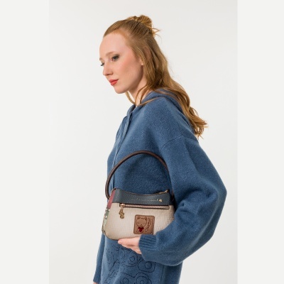 Mulher de cabelo ruivo com camisola azul segurando mala bege e preta com padrão floral