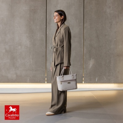 Mulher com fato castanho a segurar mala bege clara, fundo cinzento liso