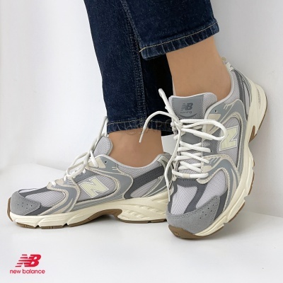 Tênis New Balance cinza claro com detalhes em branco e bege, usado com jeans escuros.