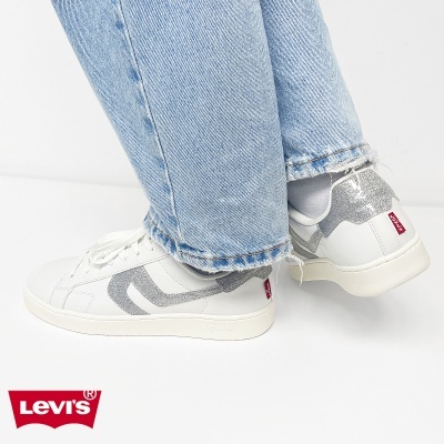 Sapatilhas brancas de couro com detalhes em glitter prateado e calças de ganga azul claro.