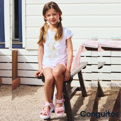 Menina de camisa branca e calções rosas sentada em mesa de piquenique branca ao ar livre