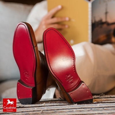 Sapatos de pele castanha com sola vermelha e detalhes metálicos no salto.