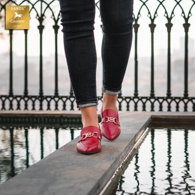 Mocassins vermelhos femininos com detalhe dourado, calças pretas e fundo com grade preta e água refletora