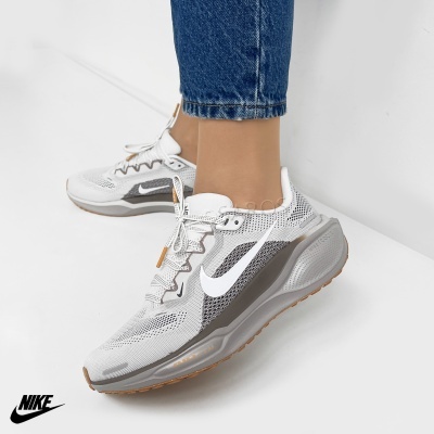 Ténis brancos e cinzentos da Nike com logótipo branco e sola castanha numa parede branca