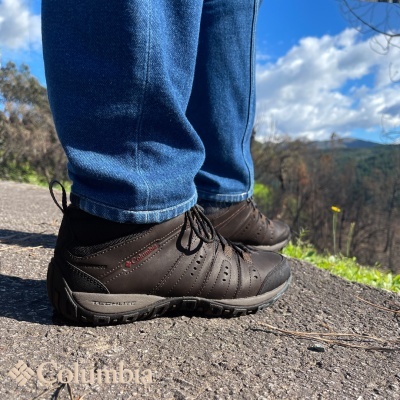 Sapatos de caminhada castanhos escuros Columbia com calças de ganga numa estrada ao ar livre