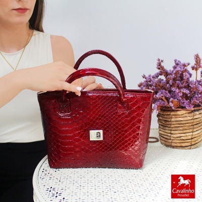 Mala de mão vermelha com padrão texturado em mesa branca junto a flores