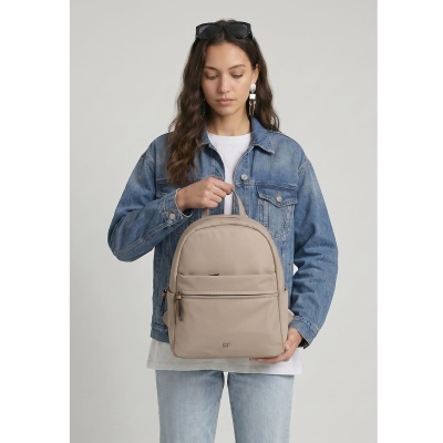 Mochila bege em material sintético com bolso frontal e logótipo SF, segurada por mulher com jaqueta jeans azul