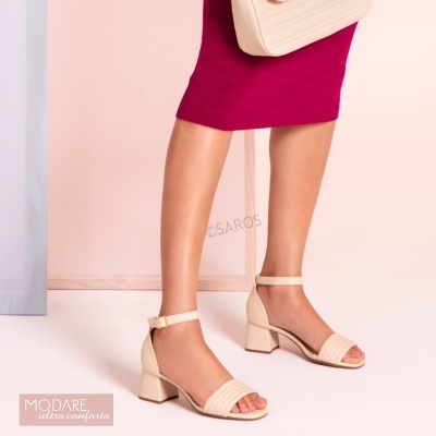 Sandálias bege de salto médio com tiras, usadas com saia rosa e bolsa bege num fundo rosa.