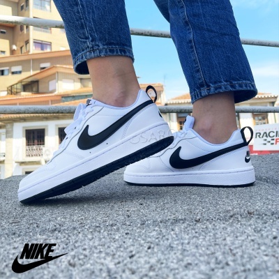 Ténis brancos Nike com Swoosh preto, sola preta, usados por pessoa com calças de ganga num ambiente urbano