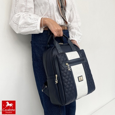 Mochila preta e branca com padrão em relevo e elementos dourados, segurada por uma pessoa