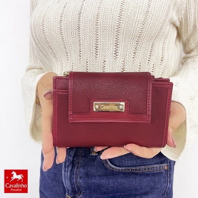 Carteira bordeaux Cavalinho segurada por pessoa com camisola branca e jeans