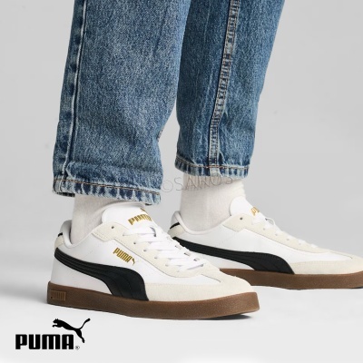 Ténis Puma brancos com risca preta e sola castanha usados com meias brancas e calças de ganga.