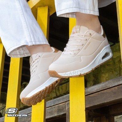 Ténis Skechers bege com sola branca e castanha suspensos em estrutura amarela