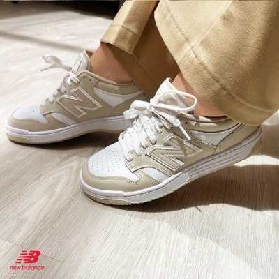 Ténis New Balance bege e branco com sola branca e bege no chão de madeira