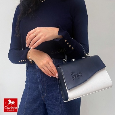 Mala bicolor azul escuro e branco em pele sintética segurada por mulher com camisola azul e calças de ganga, logótipo Cavalinho Penafiel