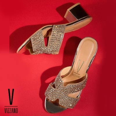 Sandálias douradas com pedras brilhantes e salto médio em bloco sobre fundo vermelho.