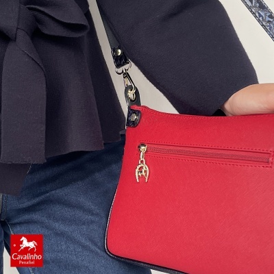 Mala de ombro vermelha com fecho dourado, usada com casaco preto e jeans azuis
