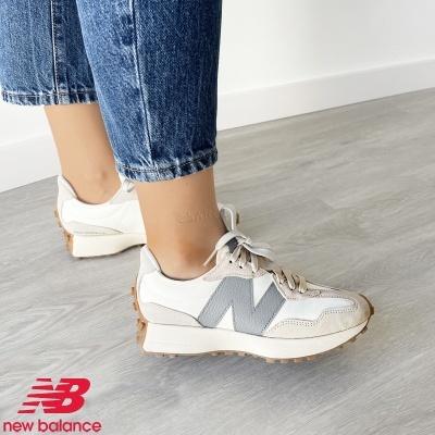 Ténis New Balance branco e cinzento com sola castanha em chão cinzento