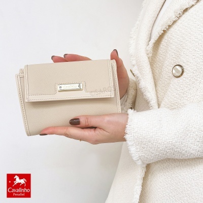 Carteira creme com placa Cavalinho, mãos femininas, casaco creme texturizado com botões