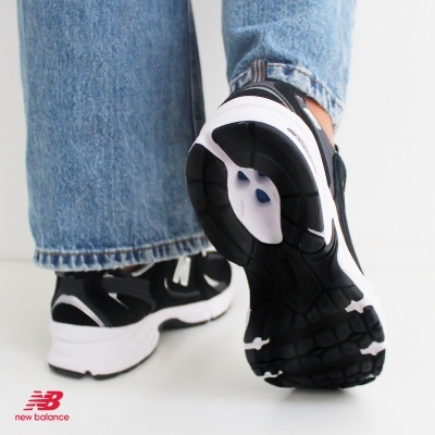 Ténis New Balance preto e branco com sola grossa, usados com calças de ganga azuis