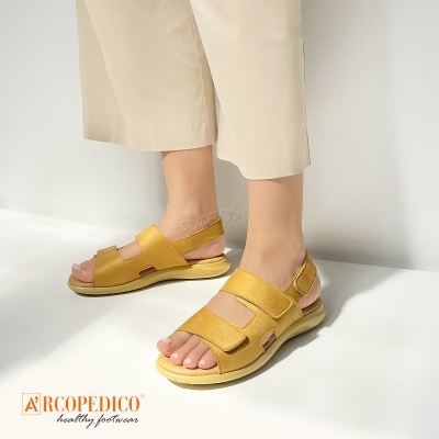 Sandálias amarelas de couro com tiras largas e fecho de velcro usadas por pessoa com calças bege