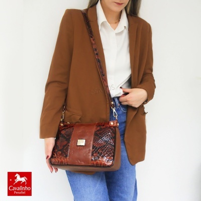 Mala de ombro em pele castanha com padrão pele de cobra castanha escura e placa metálica, usada por mulher com blazer castanho e jeans