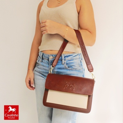 Mala Cavalinho castanha e bege com alça larga castanha, em modelo feminino com top bege e jeans