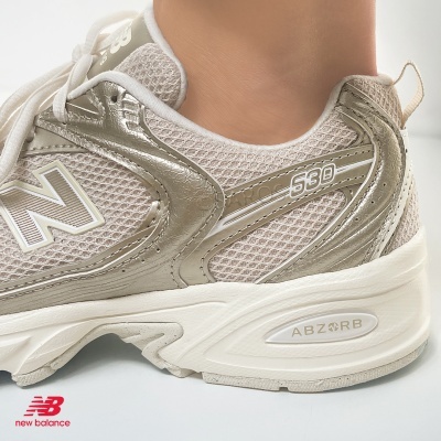 Ténis New Balance 530 bege e dourado com sola branca e logotipo ABZORB