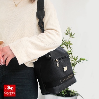Mala preta Cavalinho em textura de couro sintético com fecho dourado, usada por pessoa com camisola creme e calças pretas