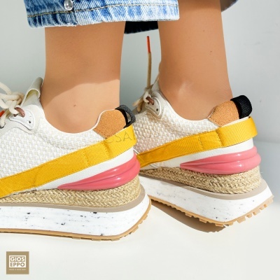 Ténis desportivos brancos com detalhes amarelo e rosa e sola branca em uso