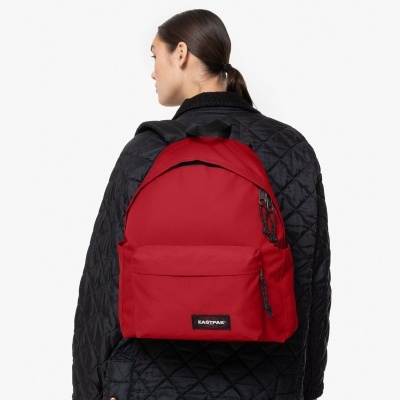 Mochila vermelho com fecho preto e etiqueta EASTPAK, usada por pessoa com casaco preto acolchoado.