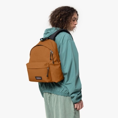 Mochila castanha Eastpak com bolso frontal e etiqueta, vista lateral com pessoa vestindo casaco azul esverdeado.