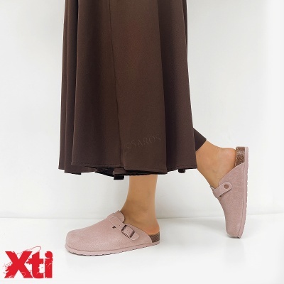 Sapatos mule rosa claro com fivela e sola antiderrapante, usados com saia castanha longa, sobre fundo branco.