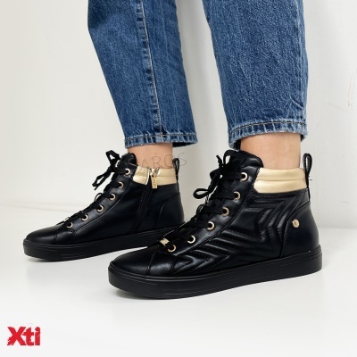 Botas pretas com detalhes bege, cadarços e fecho dourado, usadas por pessoa com calças de ganga