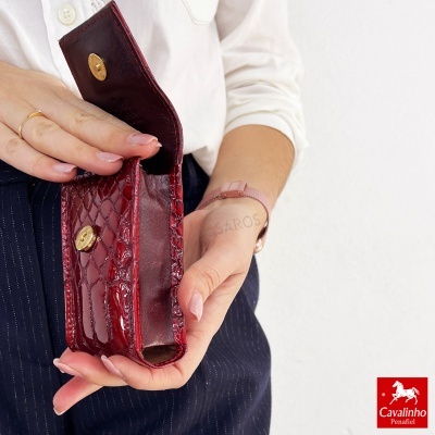 Carteira pequena vermelha de couro com textura e fecho dourado nas mãos de pessoa com camisa branca