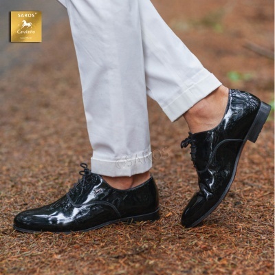 Sapatos de couro pretos brilhantes com atacadores, calças brancas, superfície de terra, logo SAROS Cavallino
