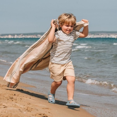 Menino a correr na praia com roupa leve e sandálias azuis