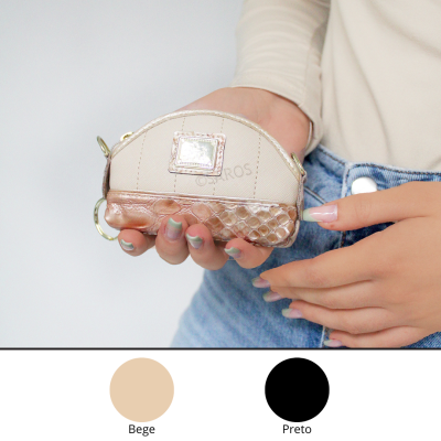 Bolsa pequena bege com textura e acabamento metálico a ouro velho, segurada por mãos femininas com unhas decoradas, fundo branco