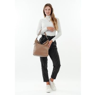 Mulher com camisola branca, calças riscas pretas, ténis brancos e mala castanha em fundo branco