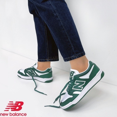 Ténis New Balance branco e verde usados por pessoa com calças de ganga azuis