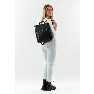 Mochila preta de pele com fecho frontal usada por mulher com jeans e camisa branca