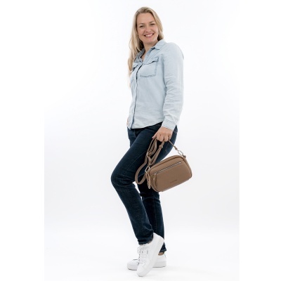 Mulher com camisa azul clara, jeans escuros, ténis brancos e mala castanha de pele