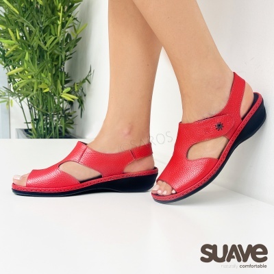 Sandálias vermelhas em pele com sola preta a ser usadas numa parede branca com planta verde ao fundo