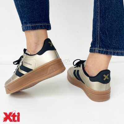 Ténis dourados com detalhes pretos e sola castanha usados com jeans azuis