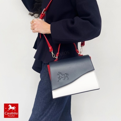 Mala Cavalinho de pele azul, branca e vermelha, usada por pessoa com casaco azul e jeans
