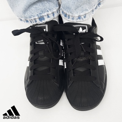 Ténis Adidas pretos com riscas brancas e atacadores pretos em fundo branco