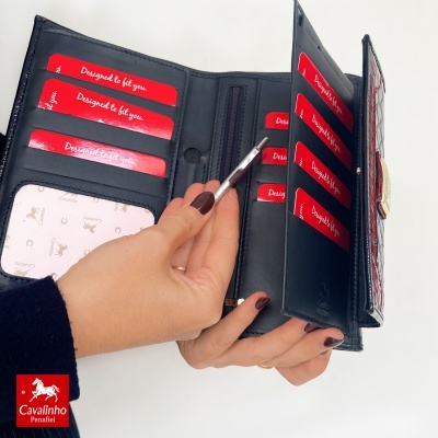 Carteira preta com interior vermelho com cartões, segurada por uma mão feminina