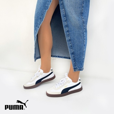 Ténis Puma brancos com detalhes azul escuro e sola castanha com pessoa a usar saia de ganga azul